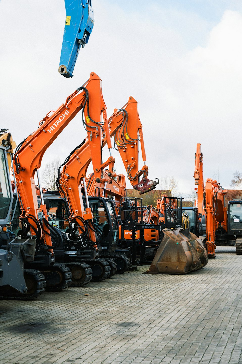 Escavatori Hitachi arancioni parcheggiati in file ordinate sull'asfalto.