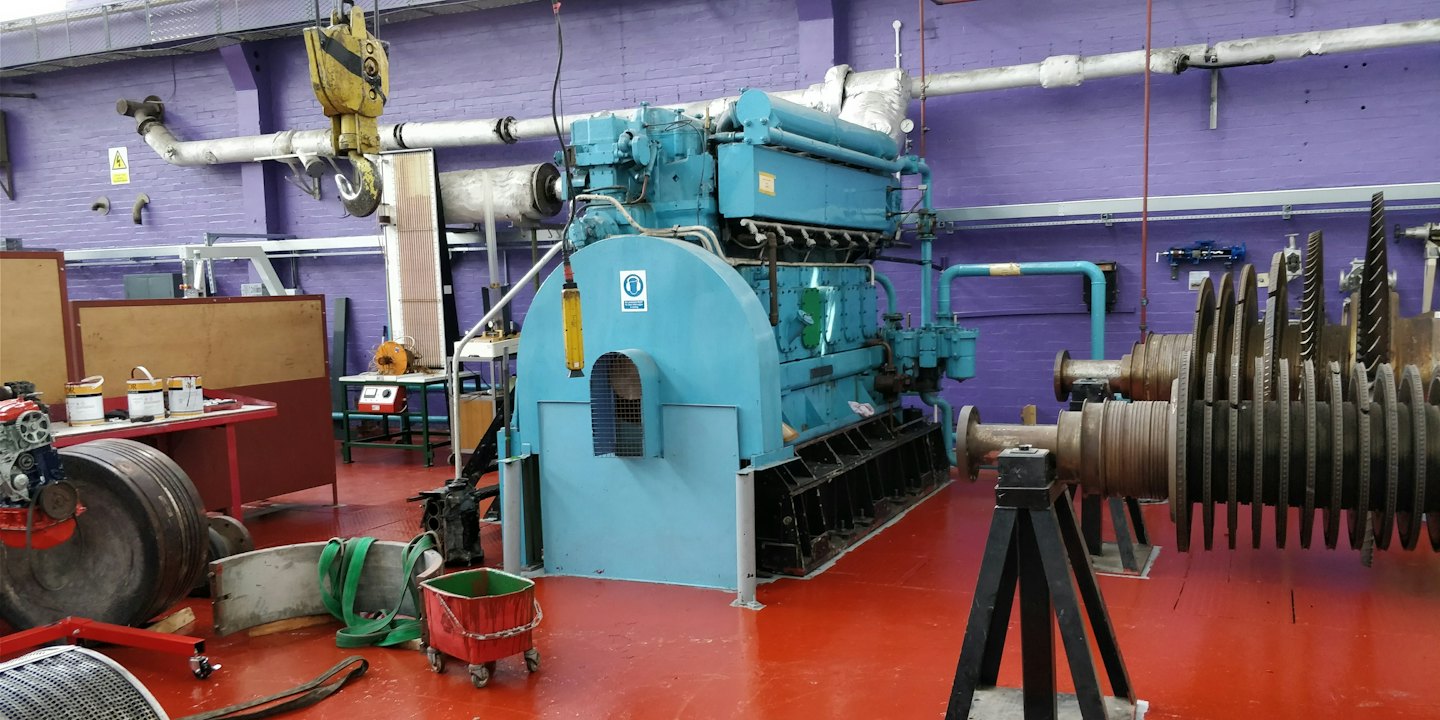 Un grande motore industriale si trova in un'officina su un pavimento rosso.