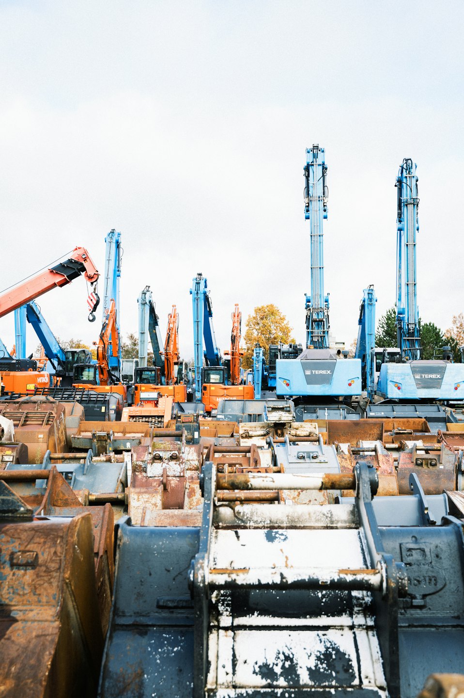 File di escavatori arancioni e blu parcheggiati in un cantiere industriale.